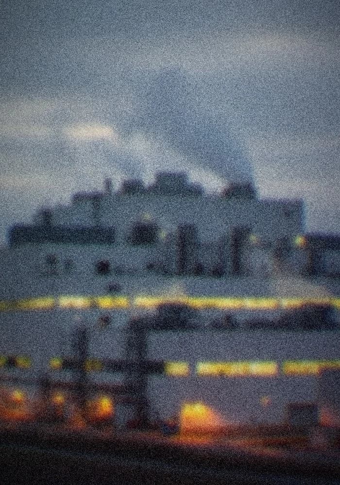 Exterior of a large silicon chip fabrication plant at dusk, steam rising from vents