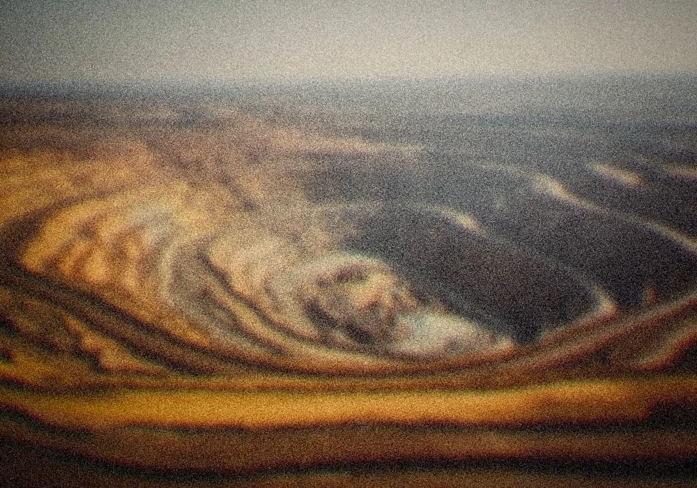 Aerial view of a vast open-pit rare-earth mineral mine, terraced ochre earth, haze in the distance