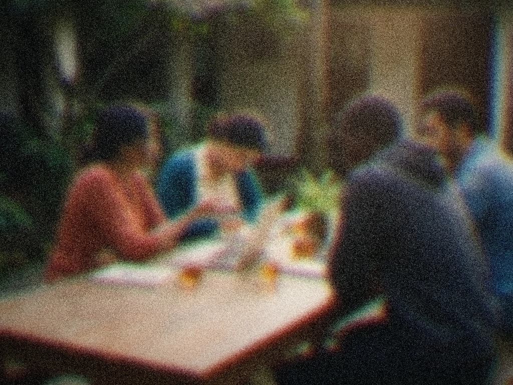 Four colleagues learning together around one laptop at a courtyard table, one explaining, the others leaning in over notebooks and chai.