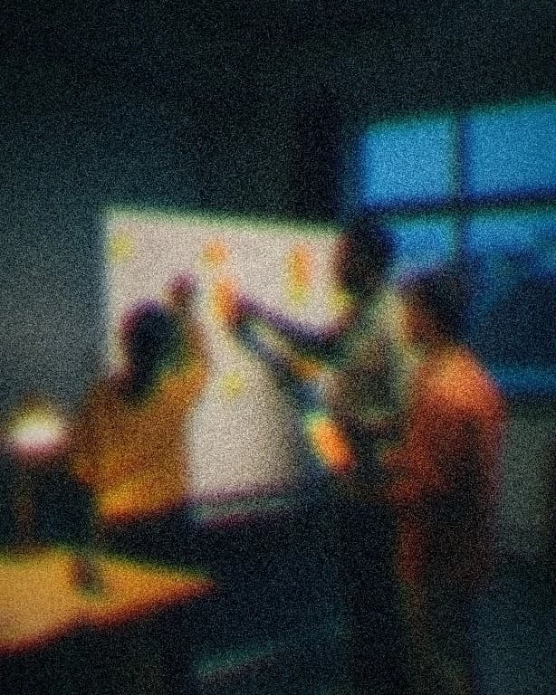 A small cross-border team mapping a product plan on a whiteboard of marker boxes and sticky notes at blue hour, seen from behind, one holding a glowing laptop.